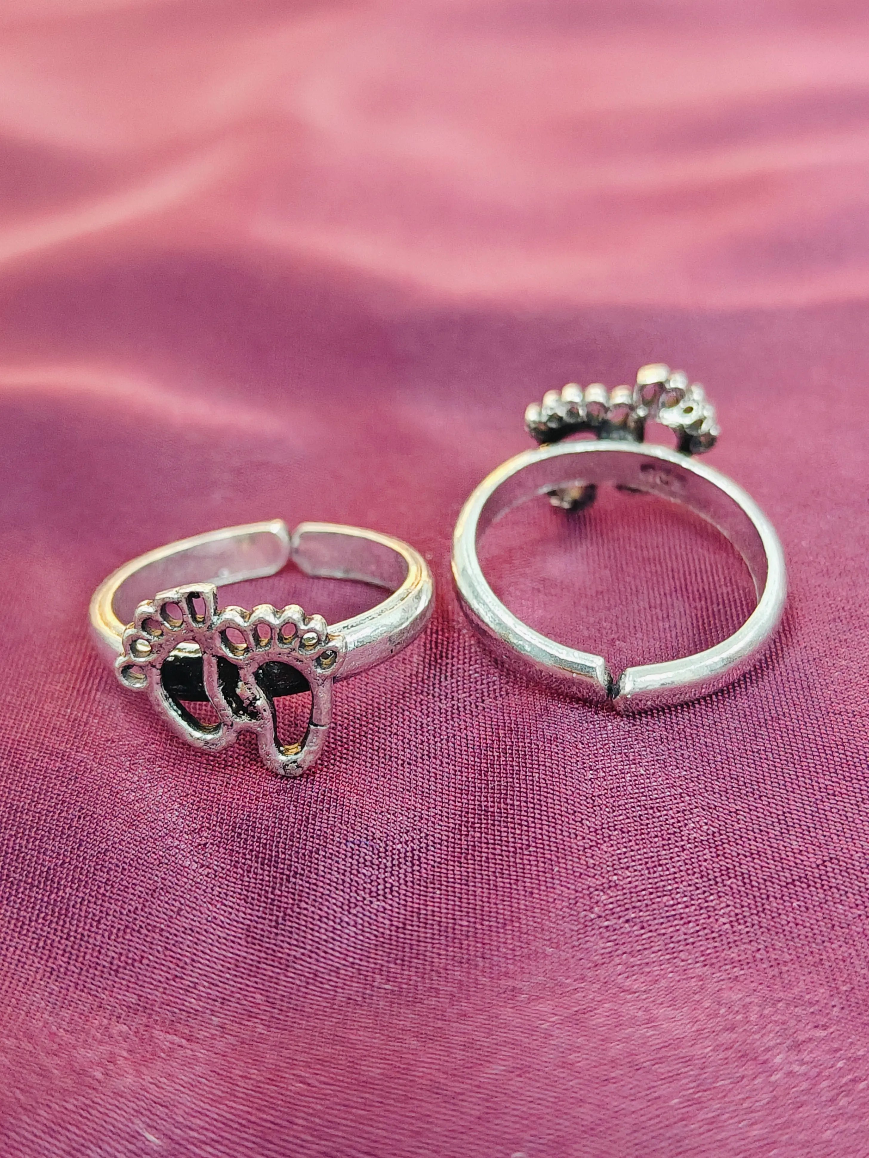 Two silver rings with paw print designs on a pink fabric background